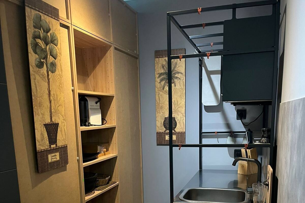 A compact kitchen with wooden cabinets, a built-in shelf, a sink, and a hanging rack.