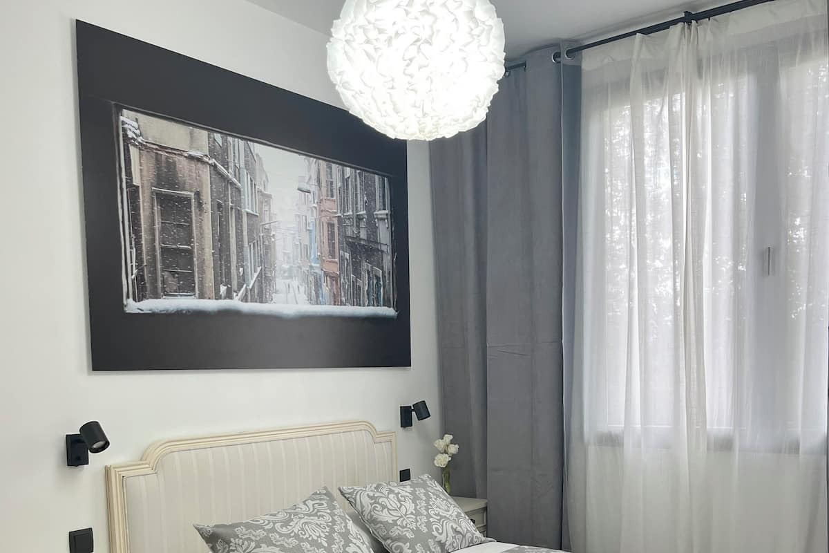 A neatly arranged bedroom with a bed, bedside tables, a hanging light fixture, and a large framed picture on the wall.