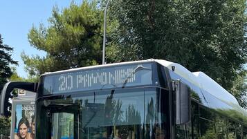 A blue bus with the number 3470, parked at a bus stop with trees in the background.