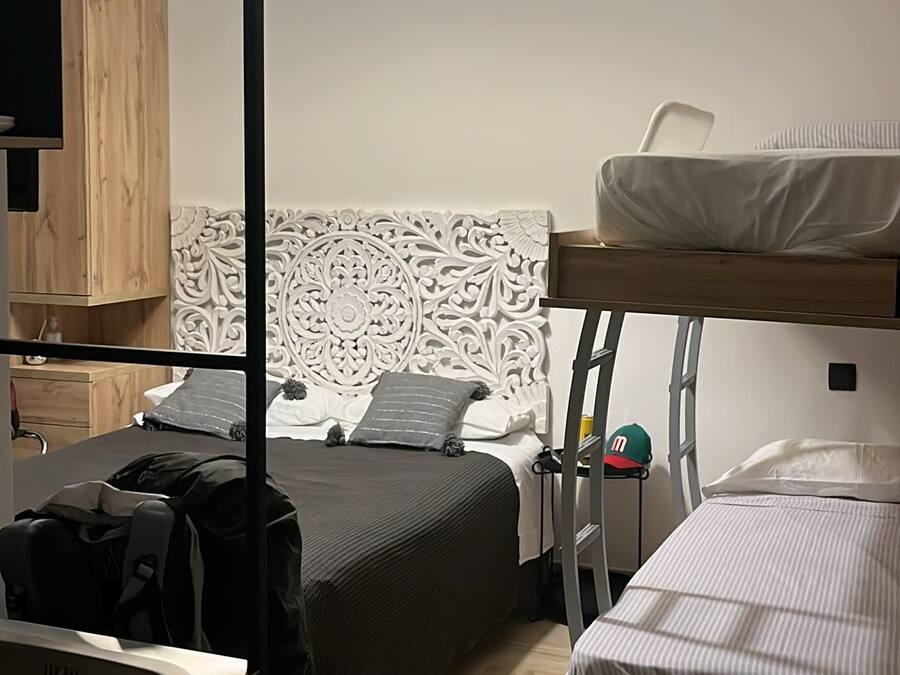 A compact dormitory room with bunk beds, a desk, and a hanging light fixture.