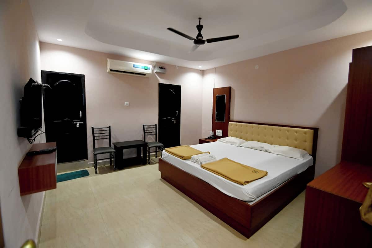 A hotel room with a bed, bedside tables, a desk, a chair, an air conditioning unit, and a ceiling fan.