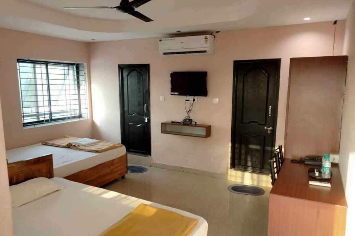 A bedroom with two beds, a TV, an air conditioner, and a ceiling fan.