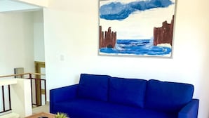 A living room with a blue sofa, a wooden coffee table, and a painting of a coastal scene. - A3 Modern apt on the Beach in Punta Cana (Punta Cana)