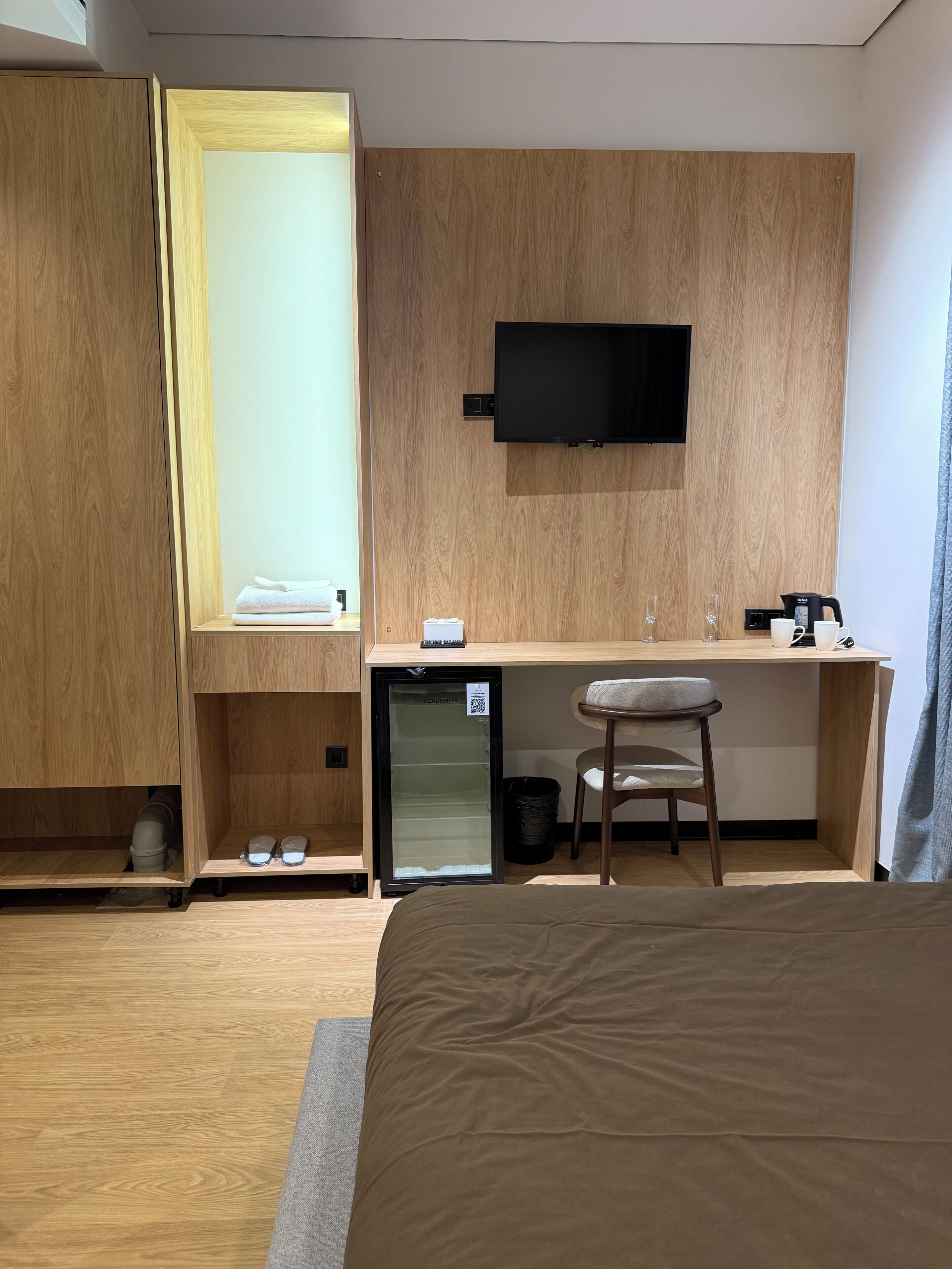 A compact hotel room with a bed, a small desk with a chair, a television, and a mini-fridge.