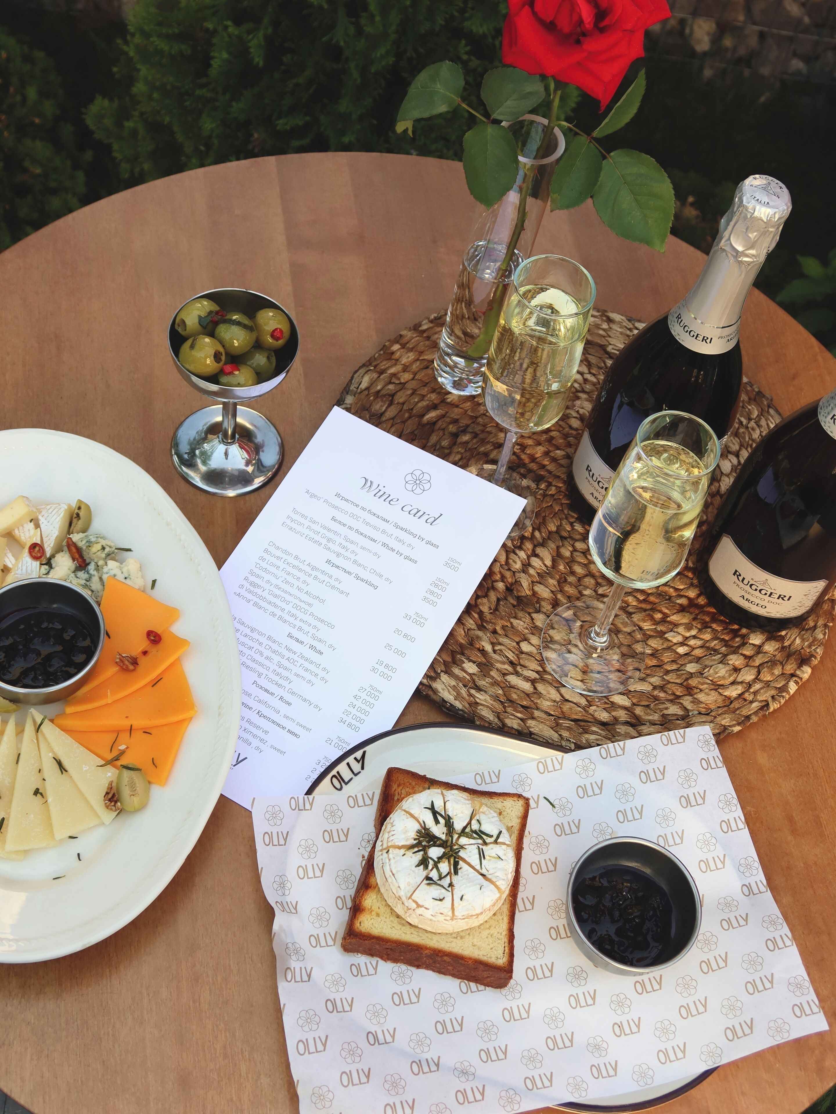A table with a wine bottle, glasses, a menu, and a plate of food.