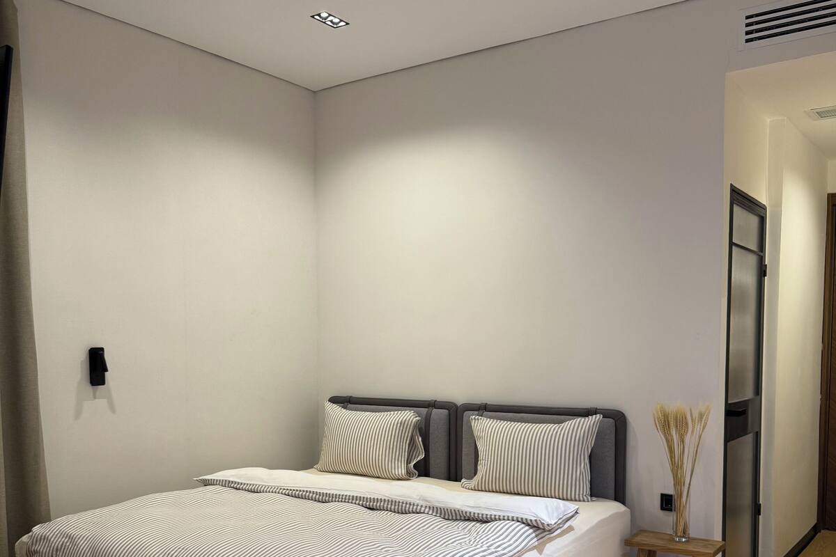 A modern bedroom with a large bed, a small wooden nightstand, and a door leading to another room.
