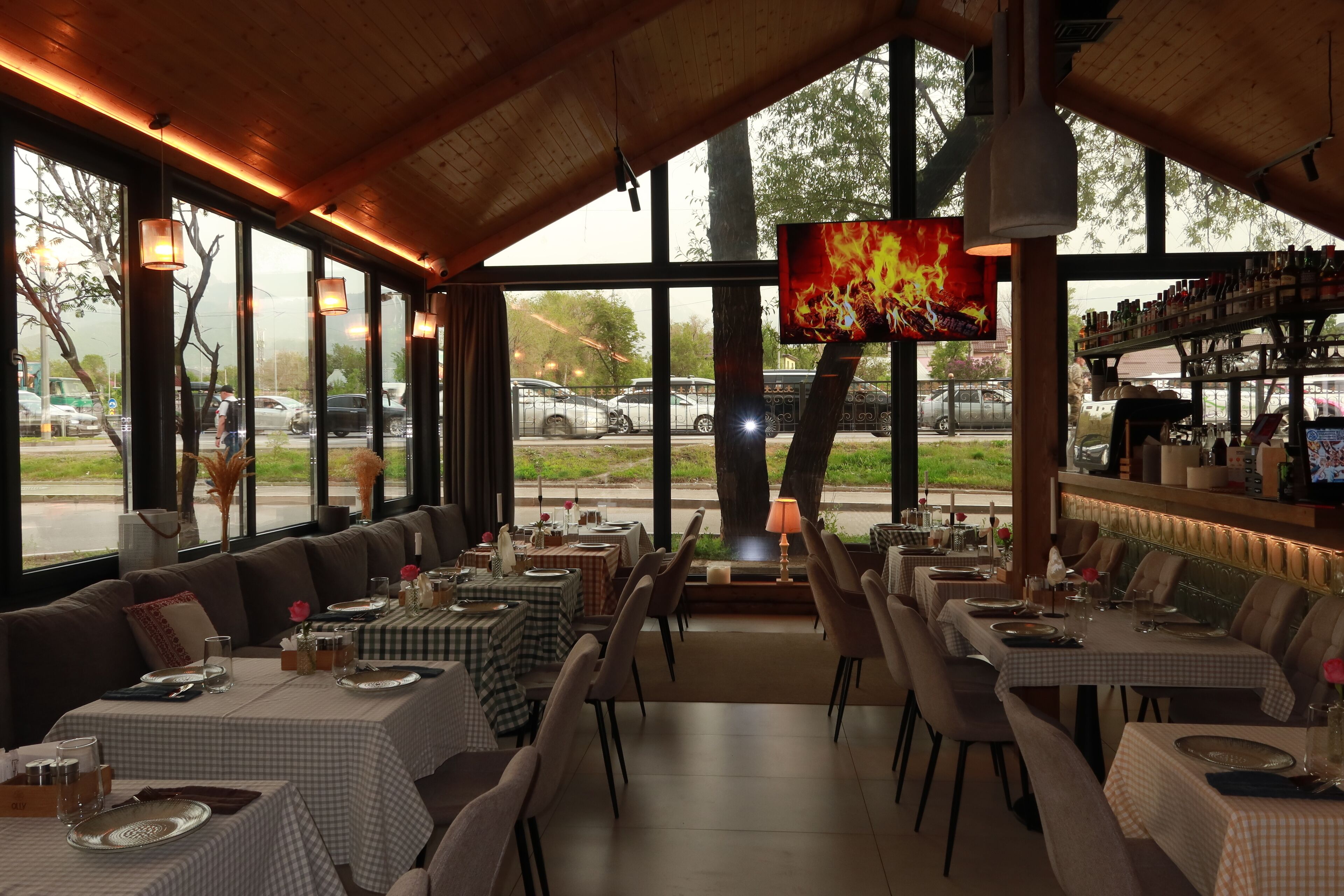 A restaurant with large windows, checkered tablecloths, and a TV screen displaying a fire.