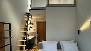 Een slaapkamer met een bed, witte kussens, een houten trap en een klein bureau.