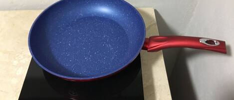 Une poêle bleue sur une plaque de cuisson à induction noire, avec un manche rouge.