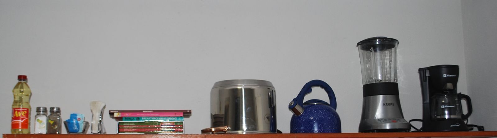 A shelf with various items including a blue kettle, a blender, a coffee maker, and some books.