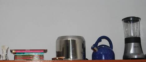 A shelf with various items including a blue kettle, a blender, a coffee maker, and some books.