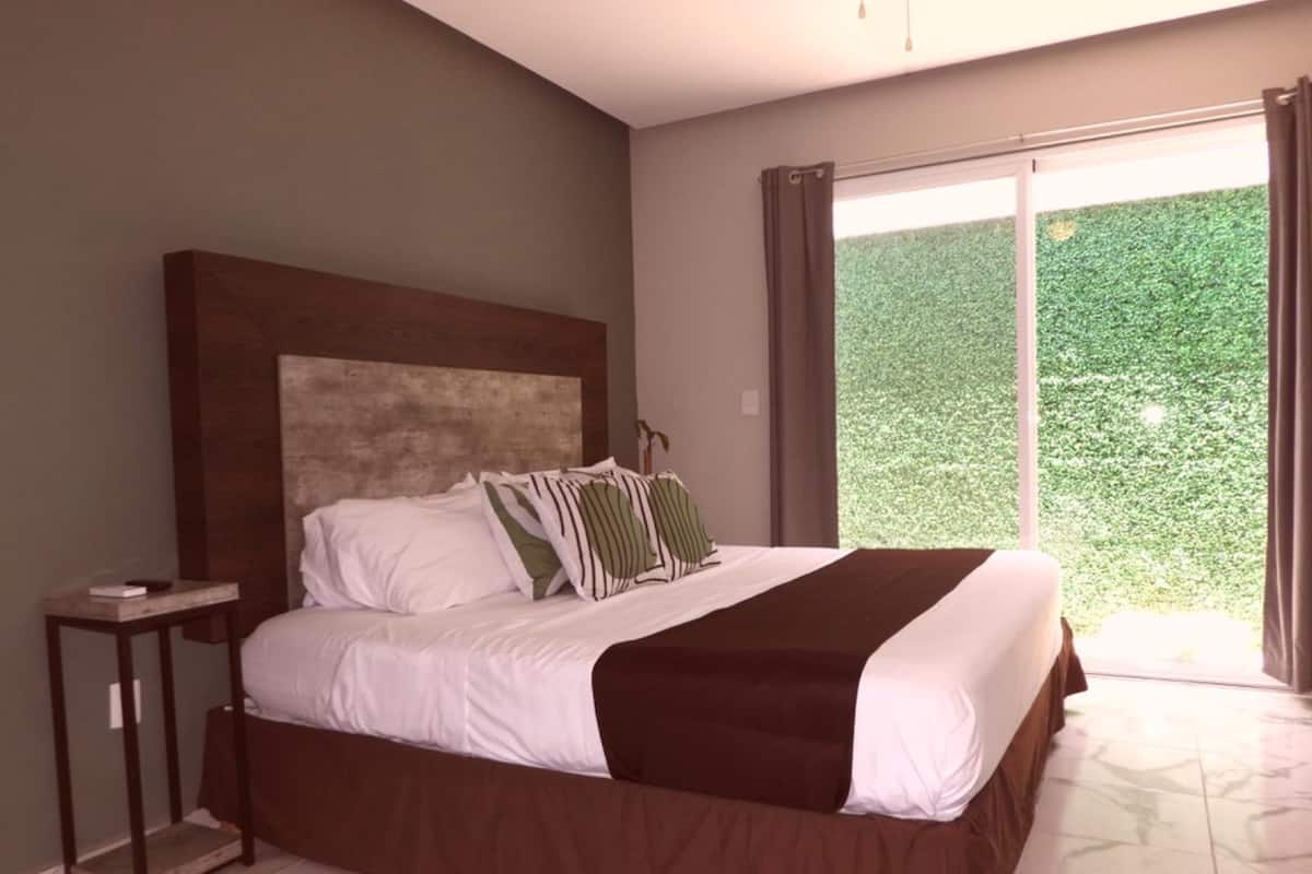Une chambre avec un grand lit, une table de chevet et une vue sur la verdure grâce à une porte-fenêtre coulissante.