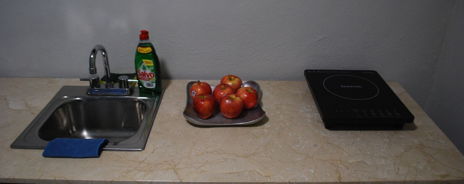 Een keukentrap met een spoelbak, een afdruiprek, een fles afwasmiddel, een bord met appels en een zwart inductiekookplaat.