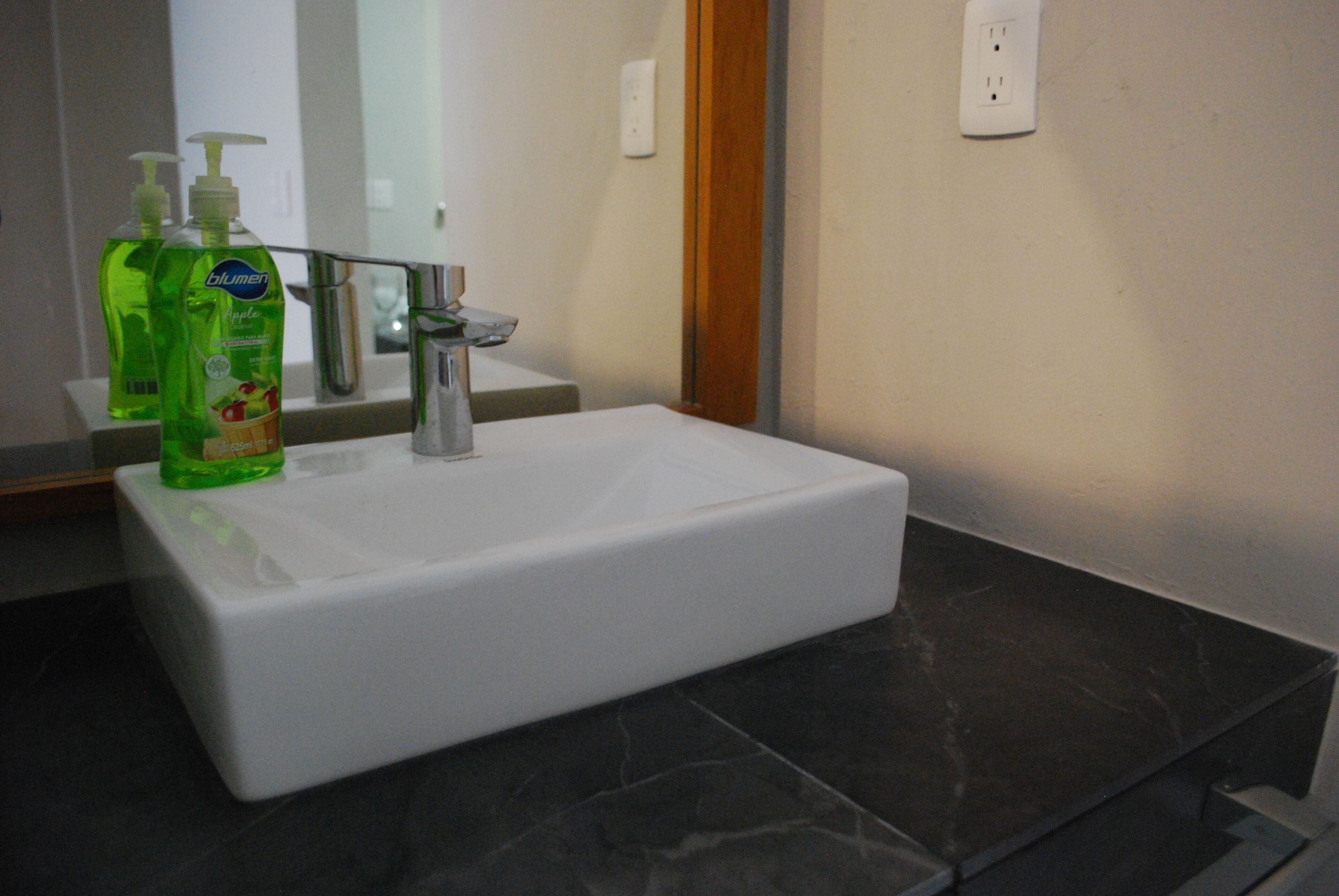 A bathroom with a white sink, green liquid soap dispenser, and a mirror above it.