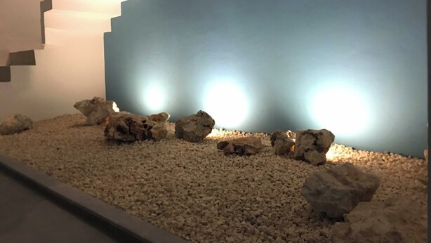 Una habitación con una escalera de diseño geométrico, pared azul y suelo de piedras.