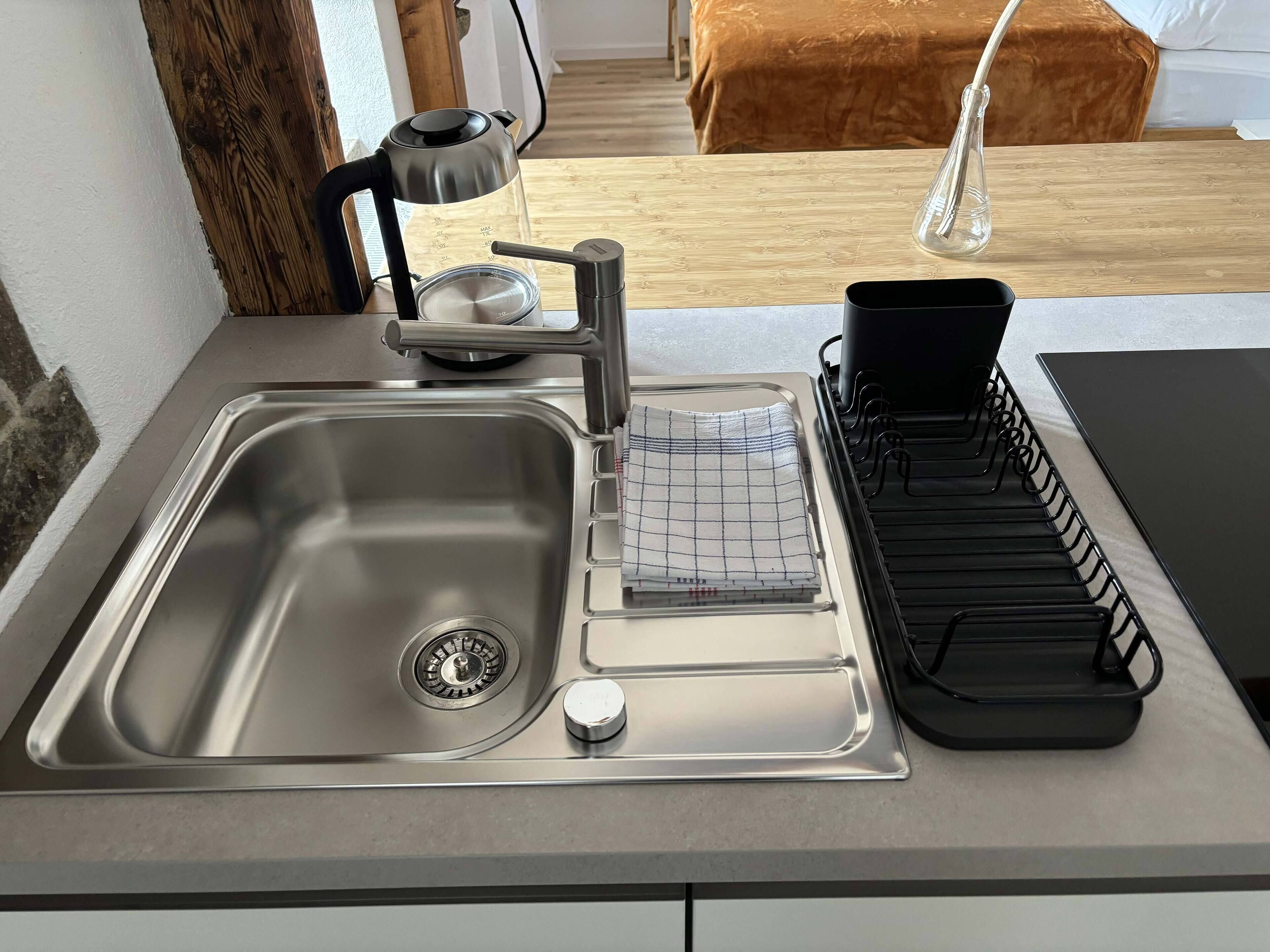 A modern kitchen with a stainless steel sink, a kettle, and a dish drying rack.