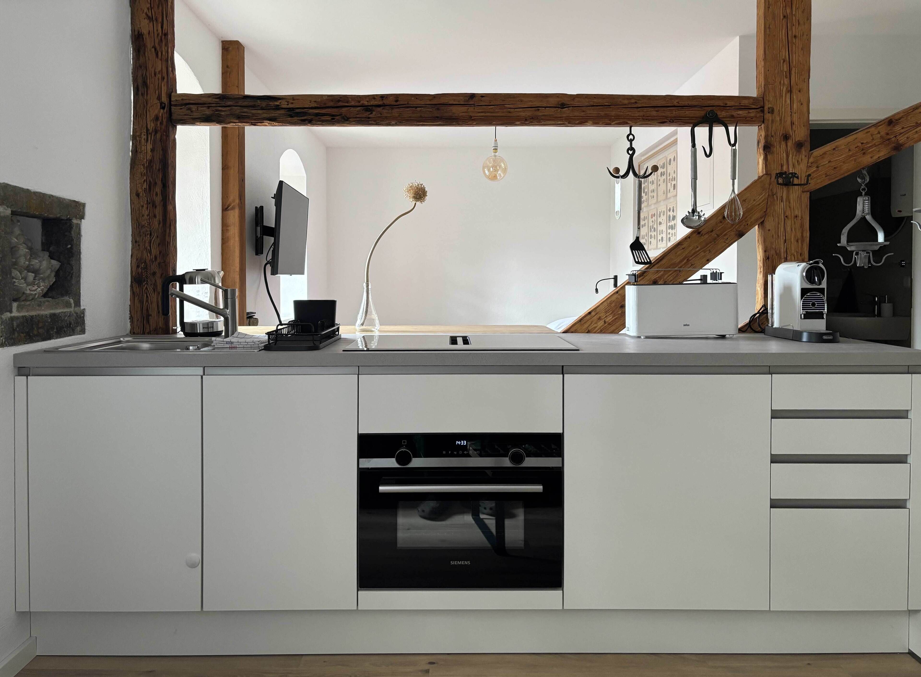 A modern kitchen with white cabinetry, a built-in oven, and a wooden beam ceiling.