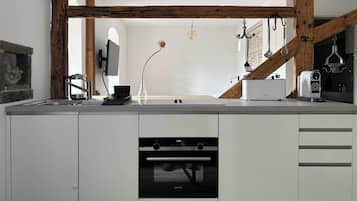A modern kitchen with white cabinetry, a built-in oven, and a wooden beam ceiling.