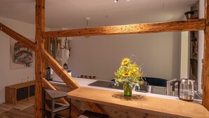 Un escalier en bois mène à une cuisine moderne située en contrebas, comprenant une table à manger, un vase avec des fleurs et une bouilloire.