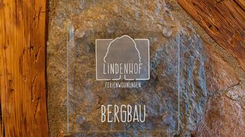 Een transparante glazen plaat met de tekst “LINDENHOF FERIENWOHNUNGEN BERGBAU” vastgemaakt aan een stenen muur.