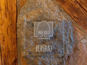 Een transparante glazen plaat met de tekst “LINDENHOF FERIENWOHNUNGEN BERGBAU” vastgemaakt aan een stenen muur.