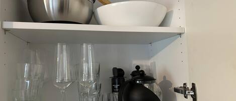 A kitchen cabinet with a stainless steel pot, a white bowl, and several clear glasses.