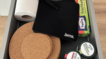 A drawer containing a black bag, two cork coasters, a roll of paper towels, a box of Toppits, and two containers of adhesive.