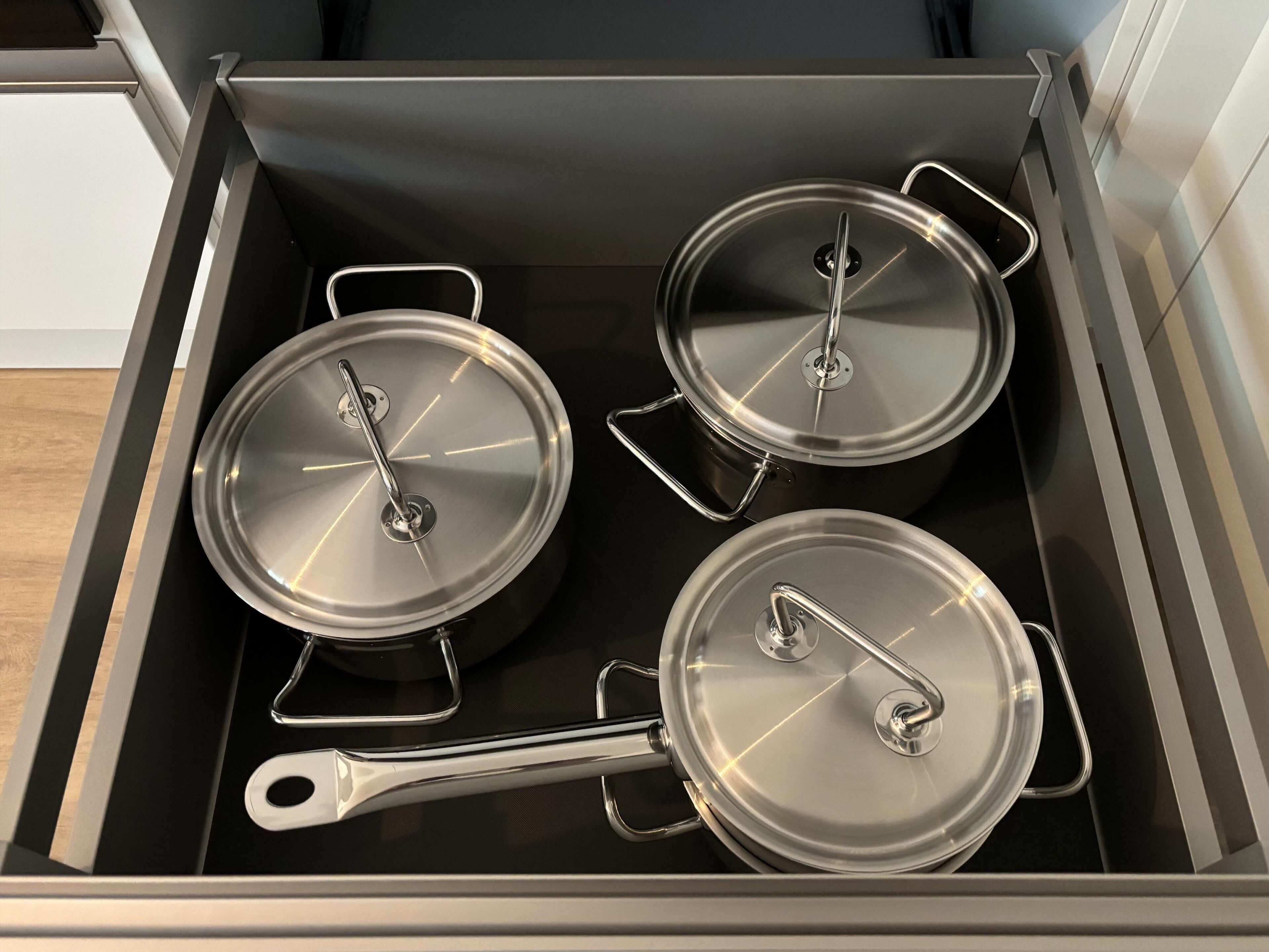 A kitchen drawer with three stainless steel pots and a ladle.