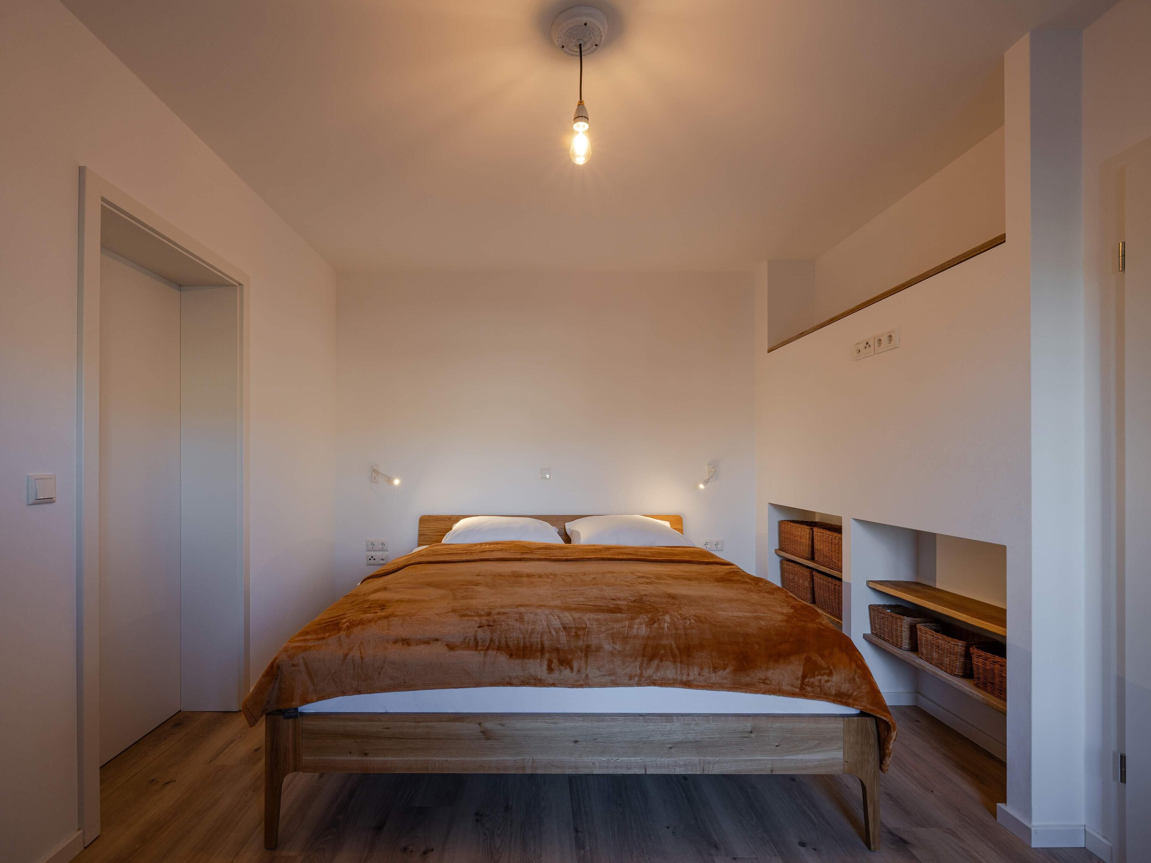 Ein Schlafzimmer mit einem Holzbett, einem Nachttisch, einem Regal mit Körben und einer Hängelampe.