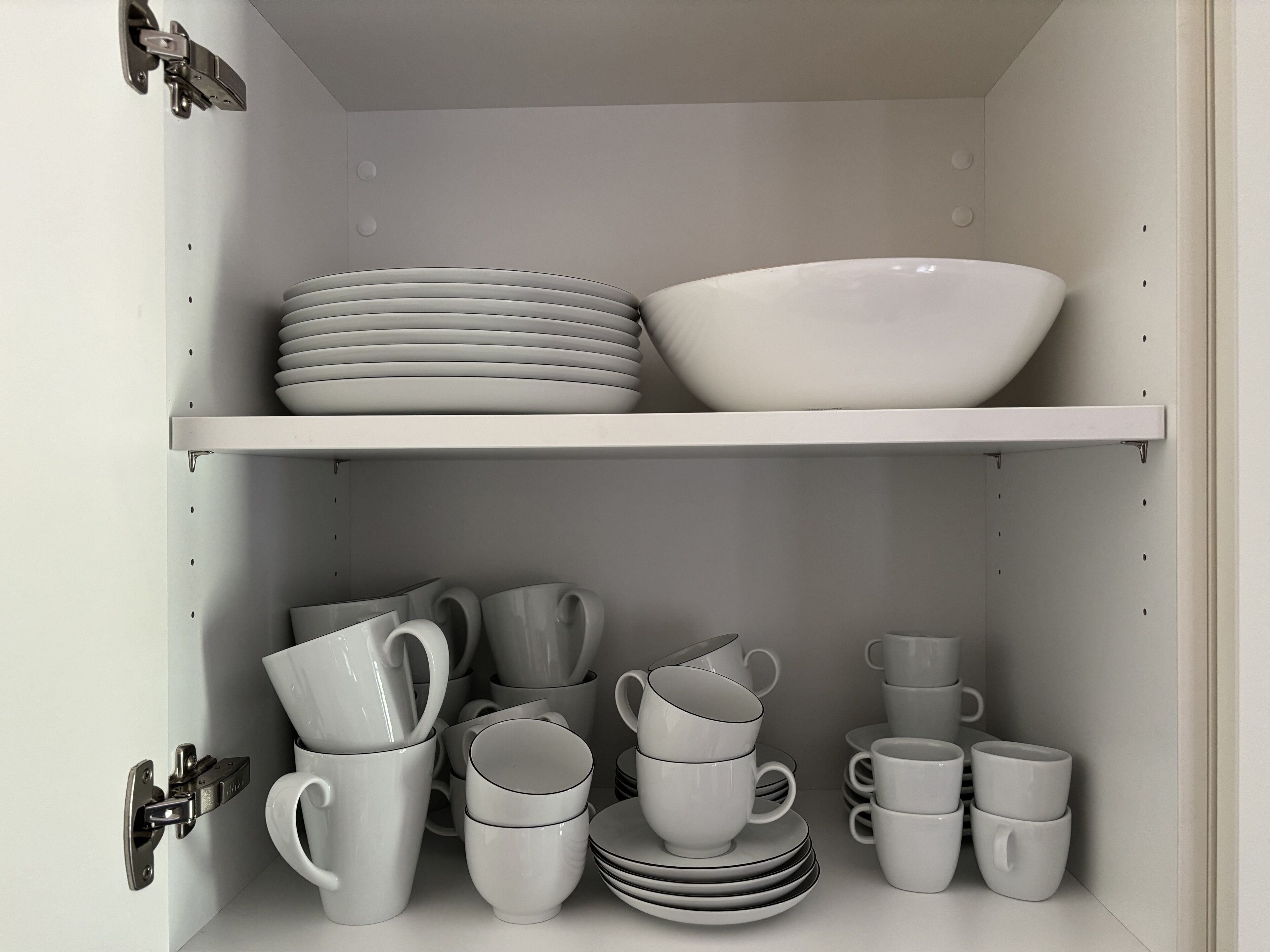 Un armario con estantes que contienen vajilla y tazas blancas.