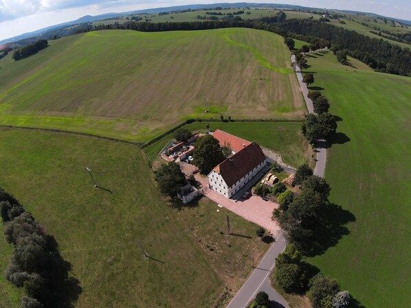 Luchtbeeld van een landelijk gelegen bezit met een groot veld, een gebouw met een rood dak en een verharde oprit.