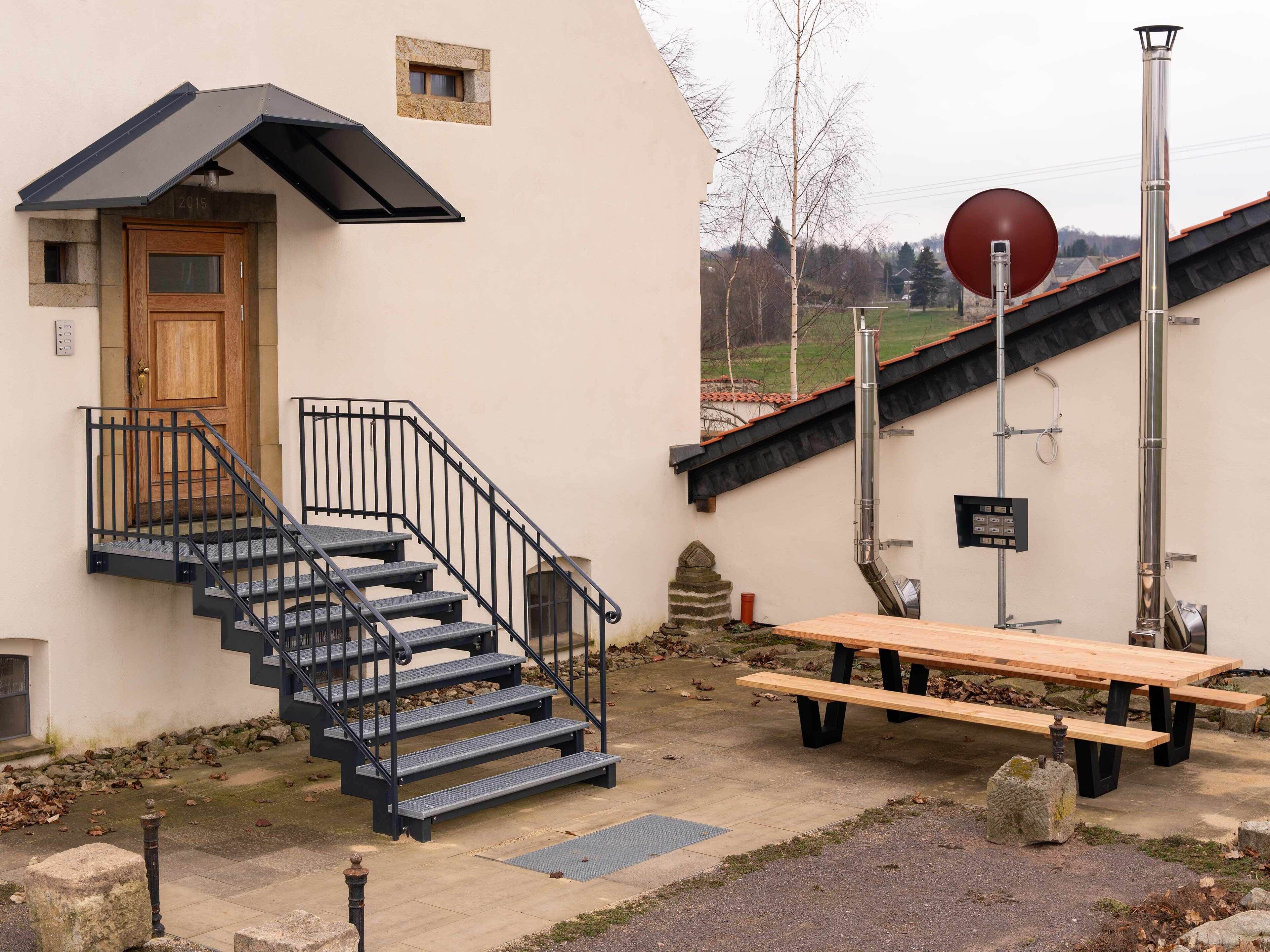 A building with a wooden door, black metal stairs, a picnic table, and a chimney.