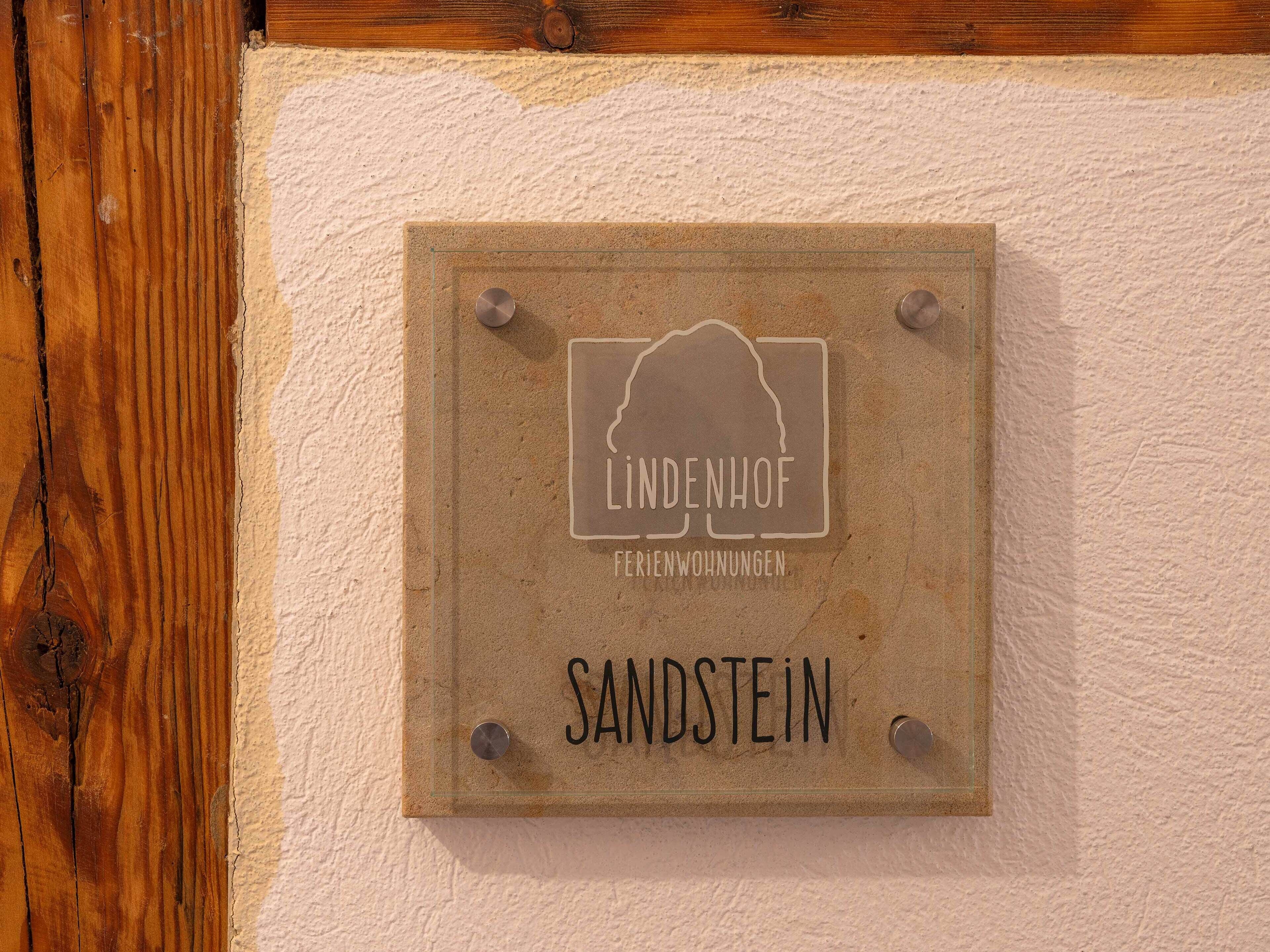 Un letrero con el texto 'LINDENHOF Ferienwohnungen Sandstein' montado en una pared.