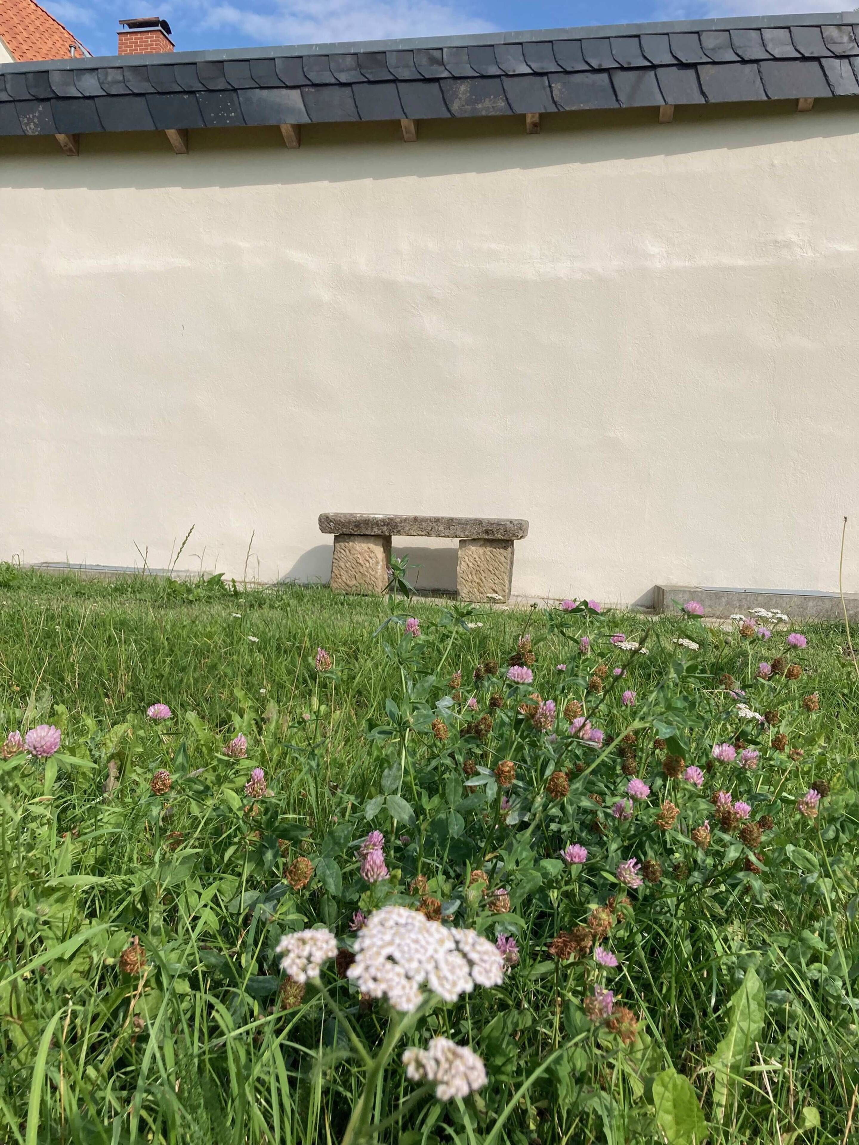 En bänk av sten framför en byggnad med ett sluttande tak.
