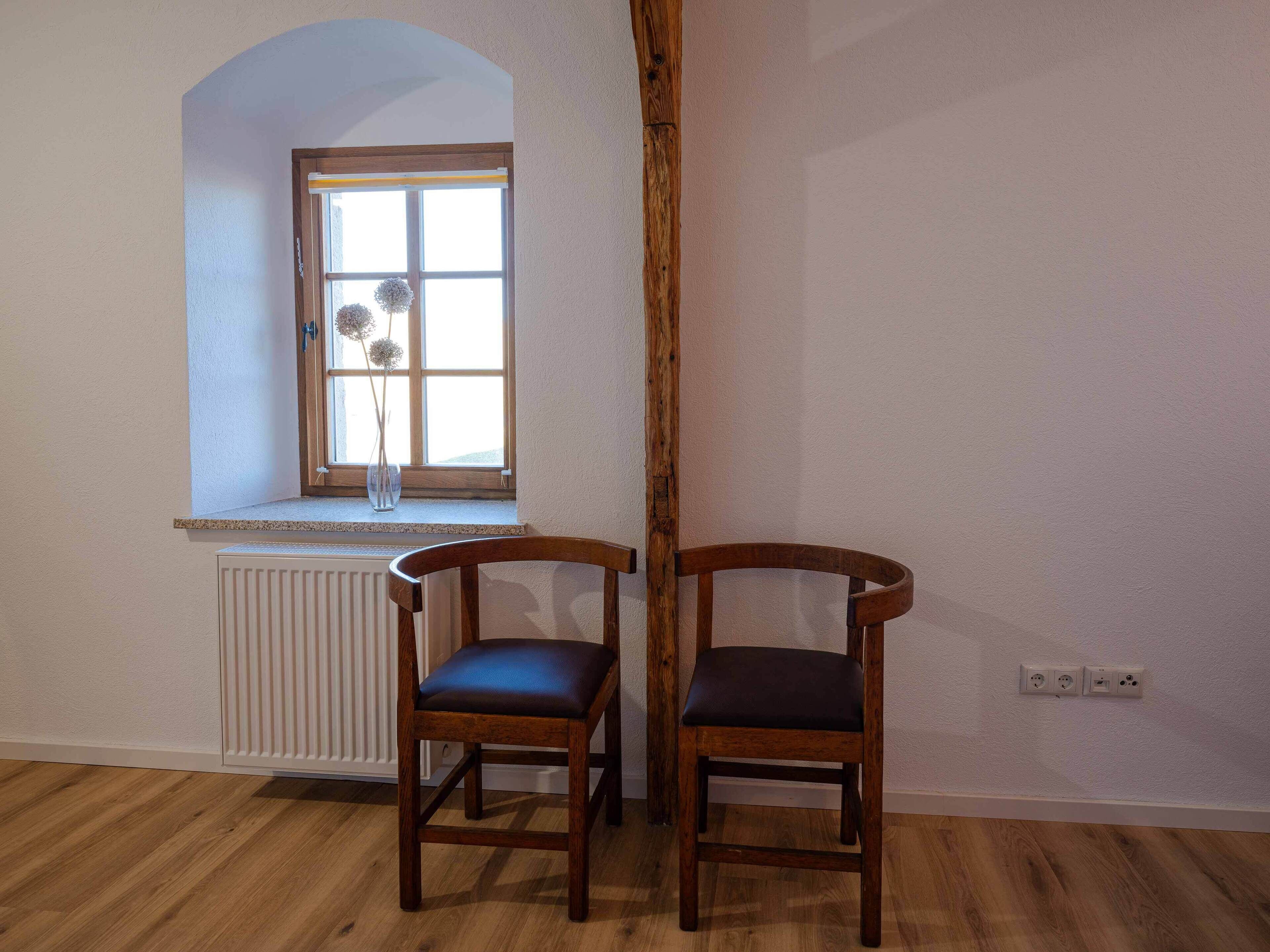 A room with two wooden chairs, a window with a view, and a radiator.