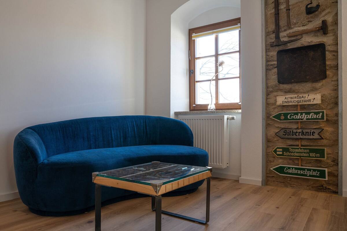 Une pièce avec un canapé bleu, une table basse en verre, un radiateur et un mur orné de panneaux de signalisation.