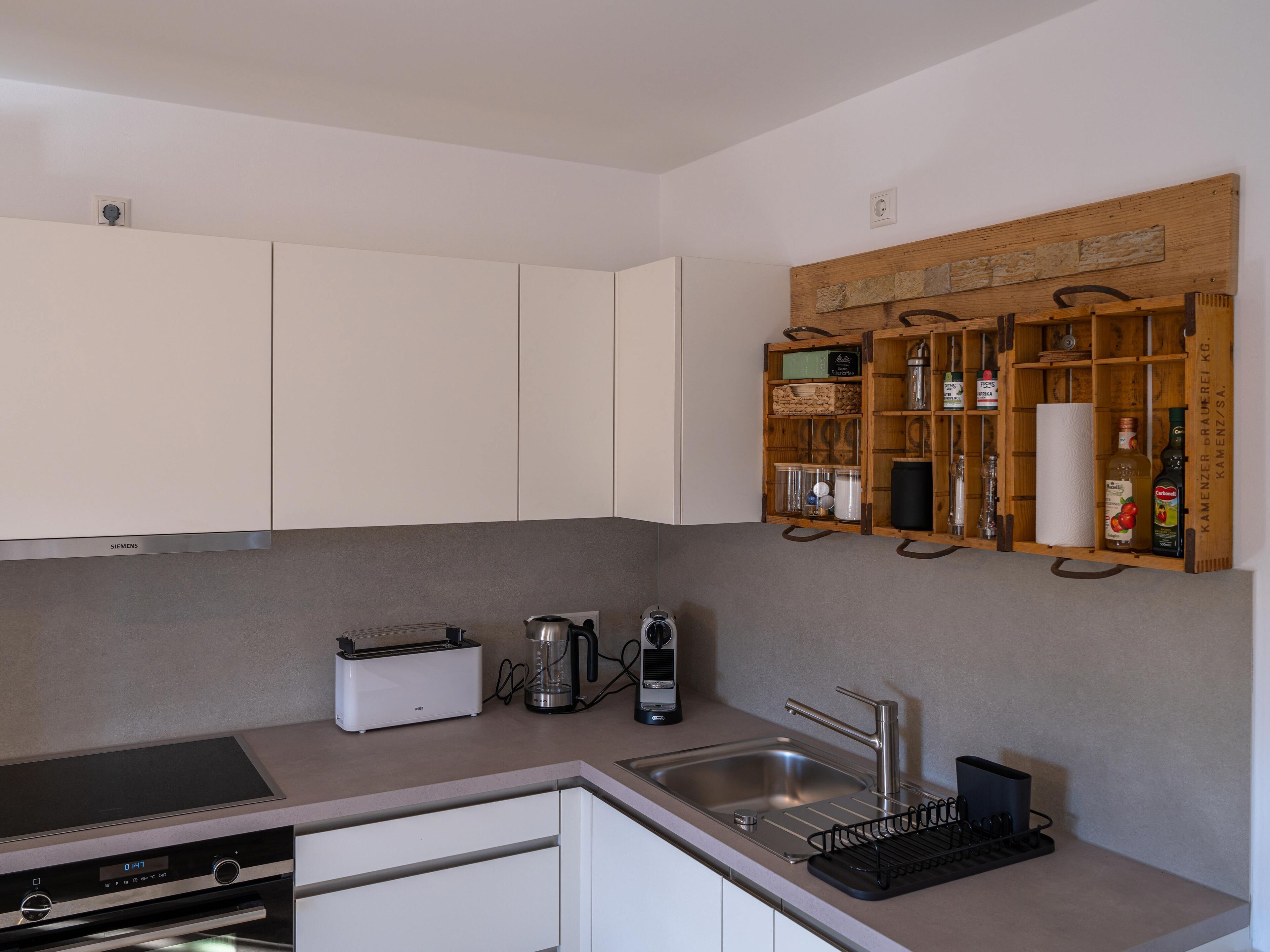 A modern kitchen with white cabinets, a built-in oven, a Siemens induction cooktop, a coffee maker, a kettle, and a wooden spice rack.