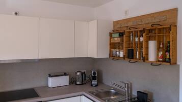 A modern kitchen with white cabinets, a built-in oven, a Siemens induction cooktop, a coffee maker, a kettle, and a wooden spice rack.