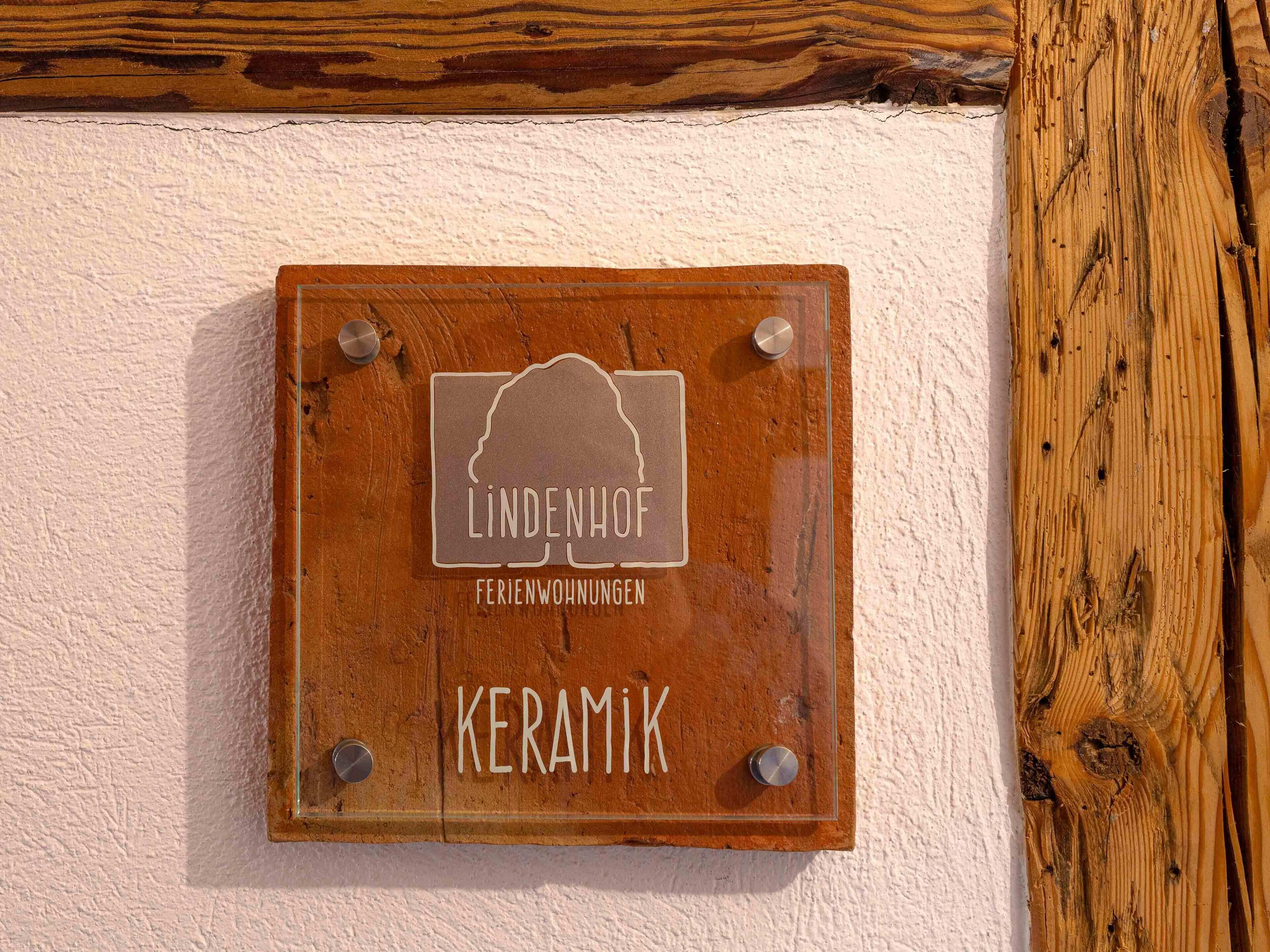 A wooden plaque with the text "LINDENHOFF FERIENWÜNGEN KERAMIK" mounted on a wall.