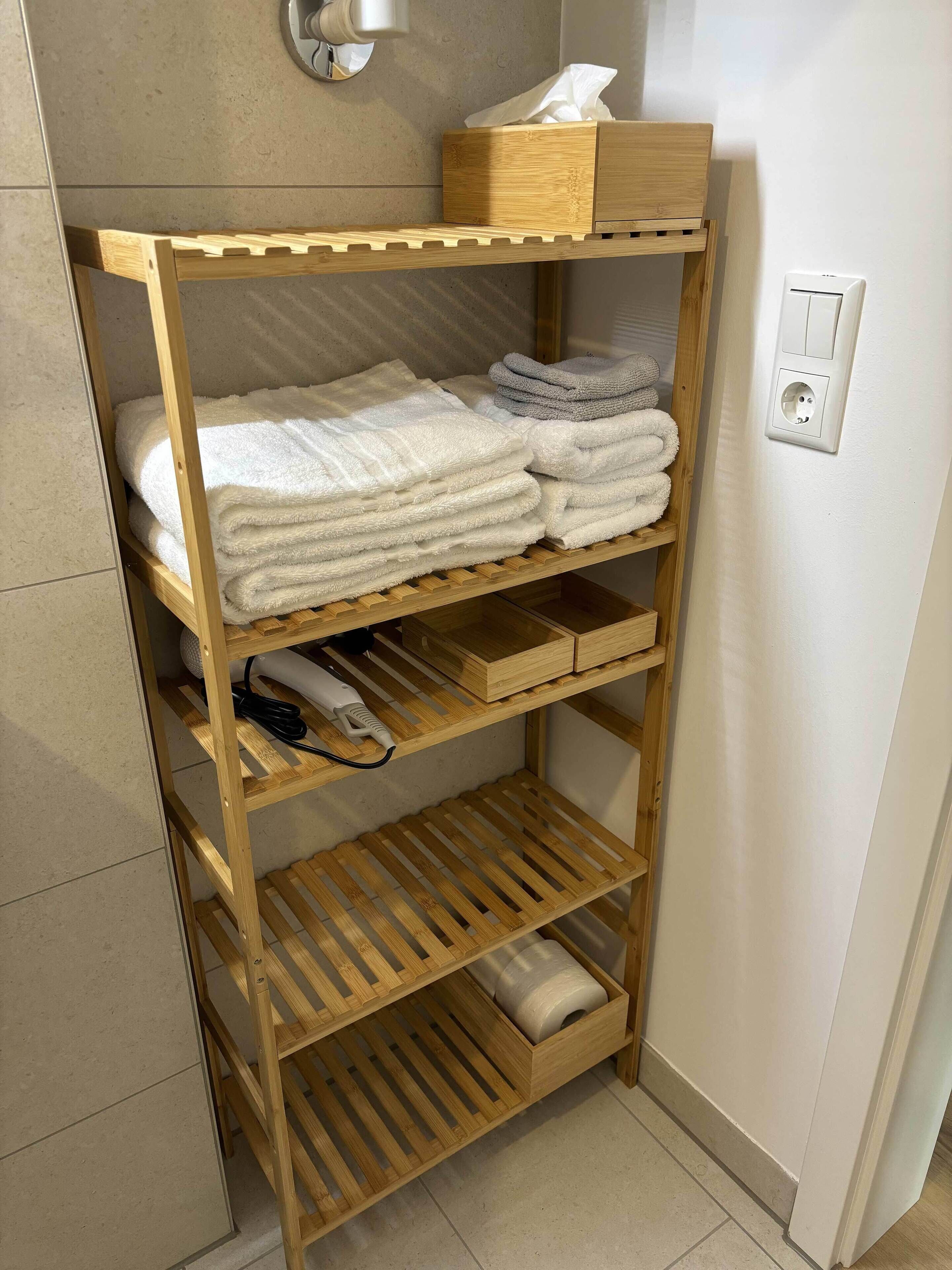 A wooden shelf unit with towels and a hairdryer.