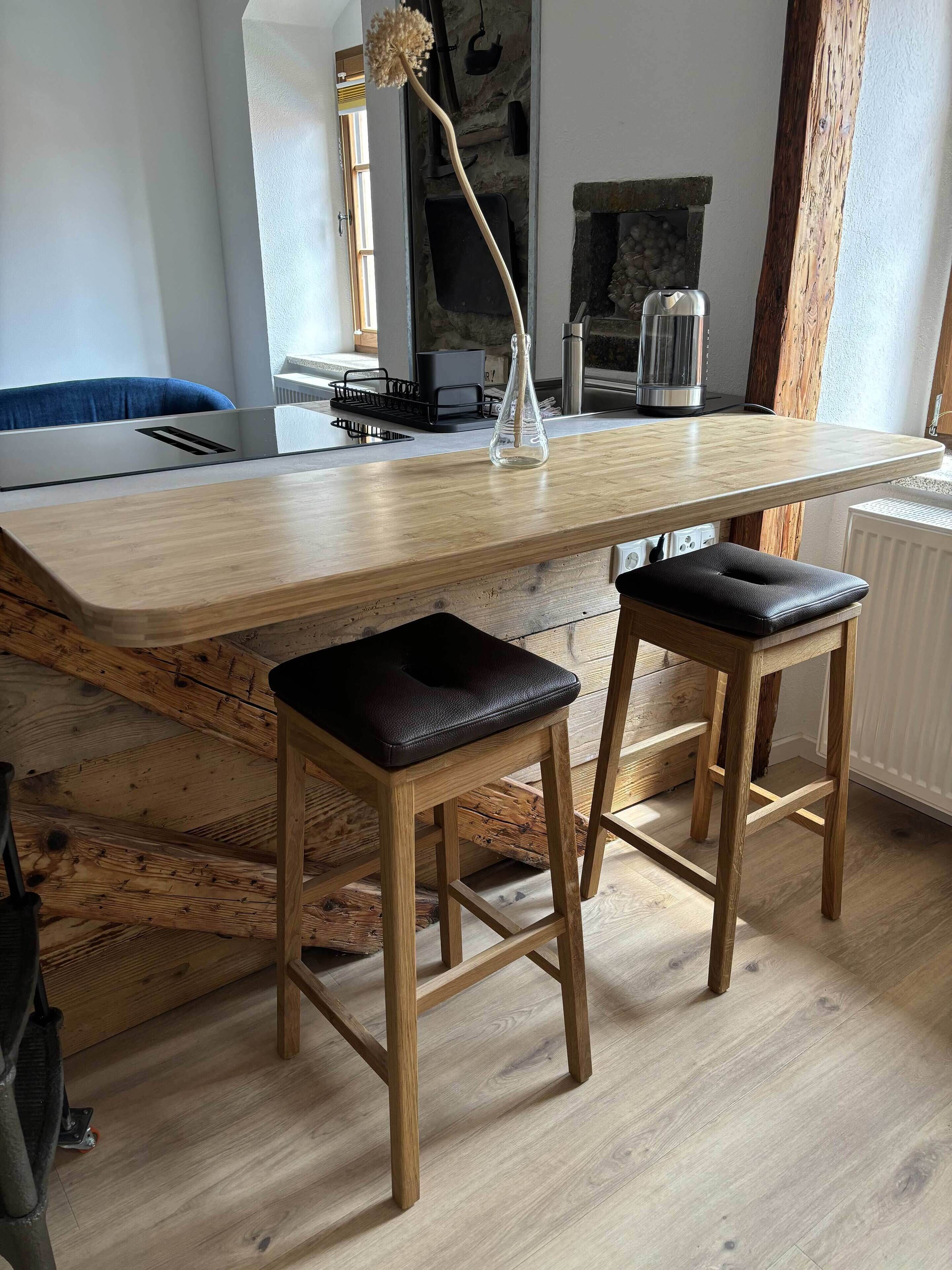 A kitchen with a wooden countertop, two stools, a hanging light, and a stone fireplace.
