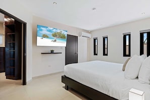 A bedroom with a bed, a TV mounted on the wall, a door, and a window.