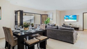 Een moderne woonkamer met een eethoek, een grijze bank, een flatscreen televisie en een grote spiegel.