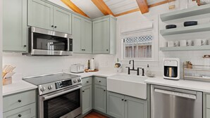 A modern kitchen with light green cabinets, stainless steel appliances, and a wooden ceiling.