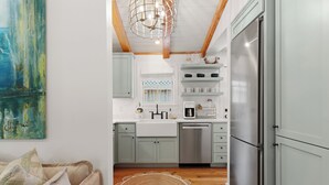 A modern kitchen with white cabinets, stainless steel appliances, and a wooden ceiling.