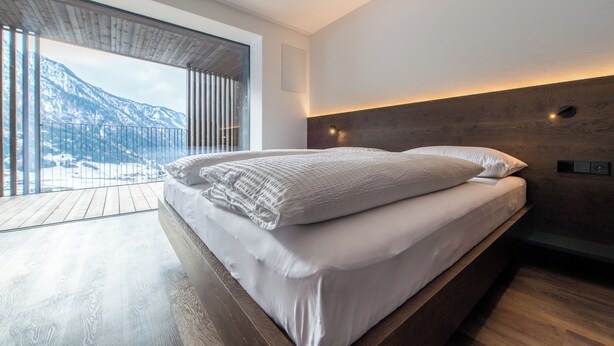 Ein modernes Schlafzimmer mit einem großen Bett, Holzböden, Blick auf Berge und einer Holzziel.