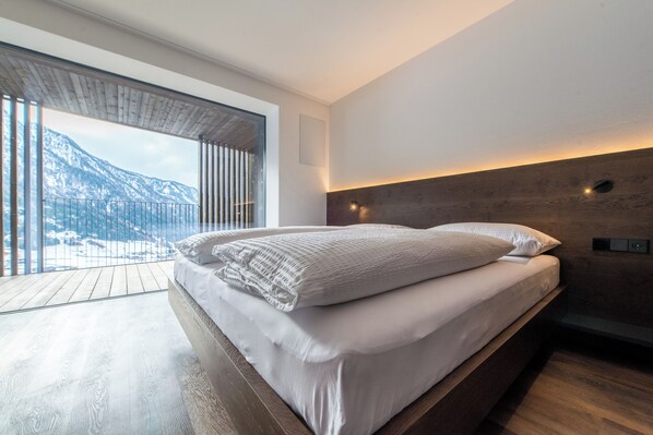 Ein modernes Schlafzimmer mit einem großen Bett, Holzböden, Blick auf Berge und einer Holzziel.