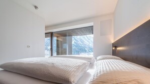 Ein modernes Schlafzimmer mit zwei Betten, großen Fenstern und Bergblick.