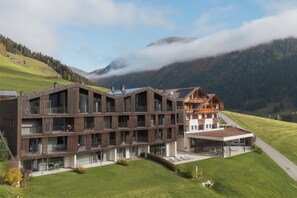 Un edificio moderno de varios pisos con balcones, ubicado en una colina con vista a la montaña.