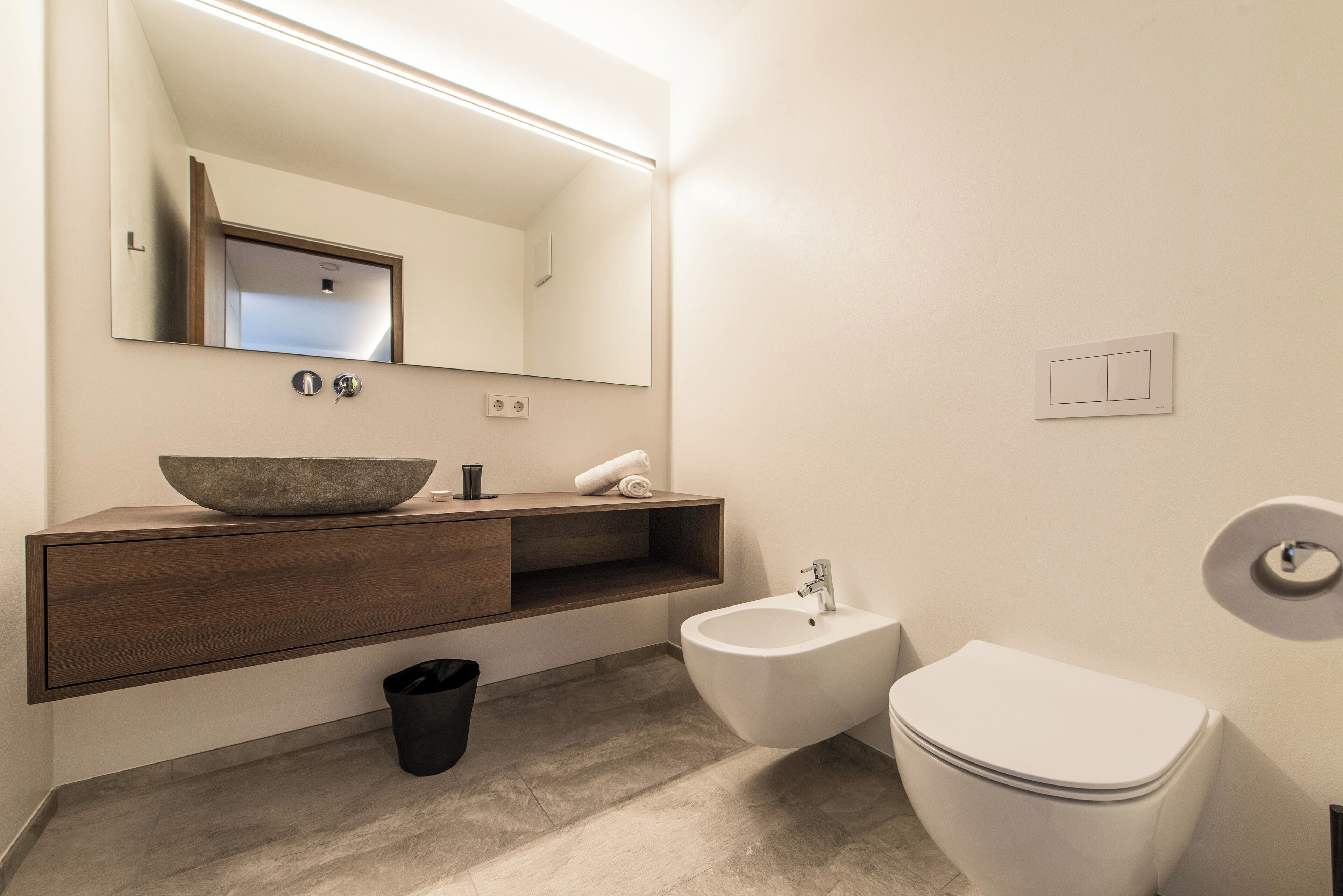 Un bagno moderno con uno specchio grande, un mobile bagno in legno, un bidet e un water.